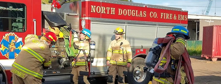 Firefighters near a fire truck, likely in a training or preparation scenario.