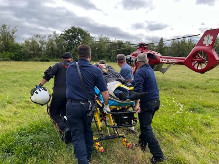 Emergency responders transporting a patient to a medical helicopter in a grassy field.