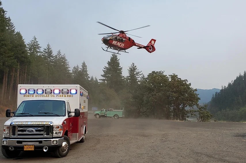 Ambulance on the ground, medical helicopter landing, dusty terrain, emergency response scene.
