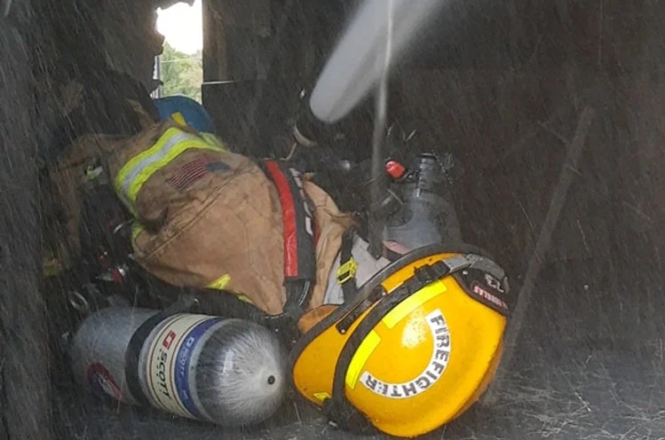 A firefighter in gear with helmet in a smoky or misty environment.