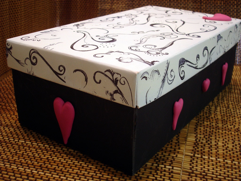 A decorative box with a white lid featuring black swirls, black base, and pink heart accents.