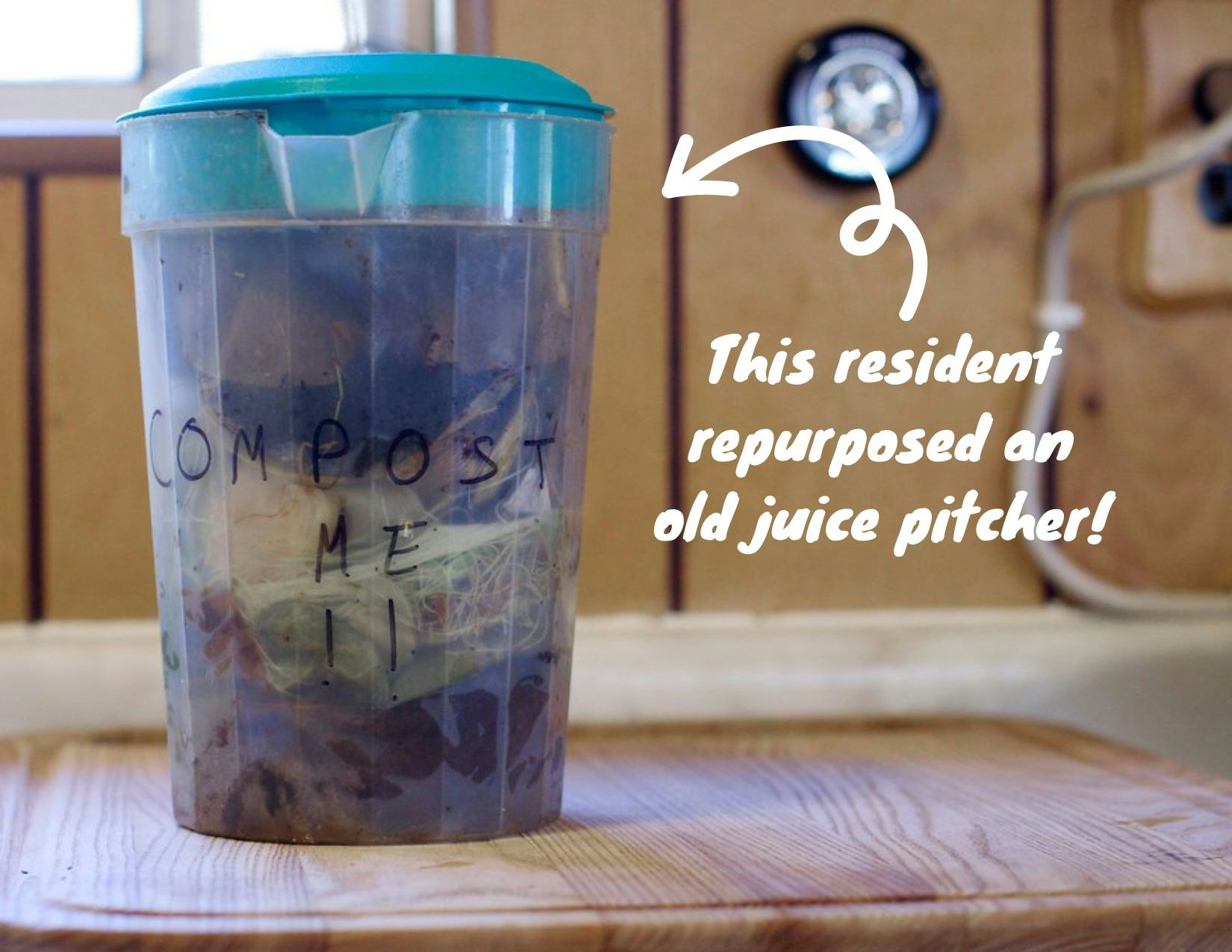 A reused juice pitcher labeled "COMPOST ME" containing organic waste, promoting recycling and composting.
