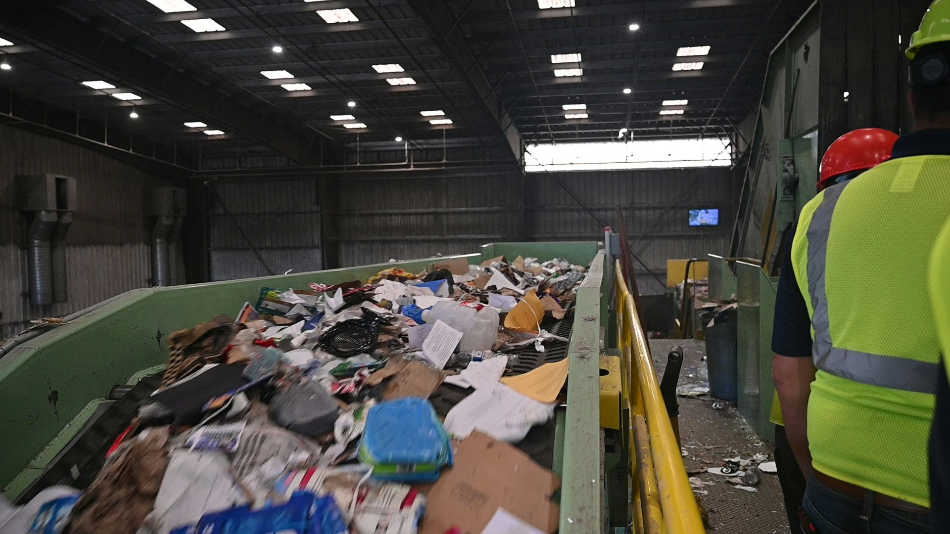 Workers overlooking a conveyor belt with assorted waste at a recycling facility.