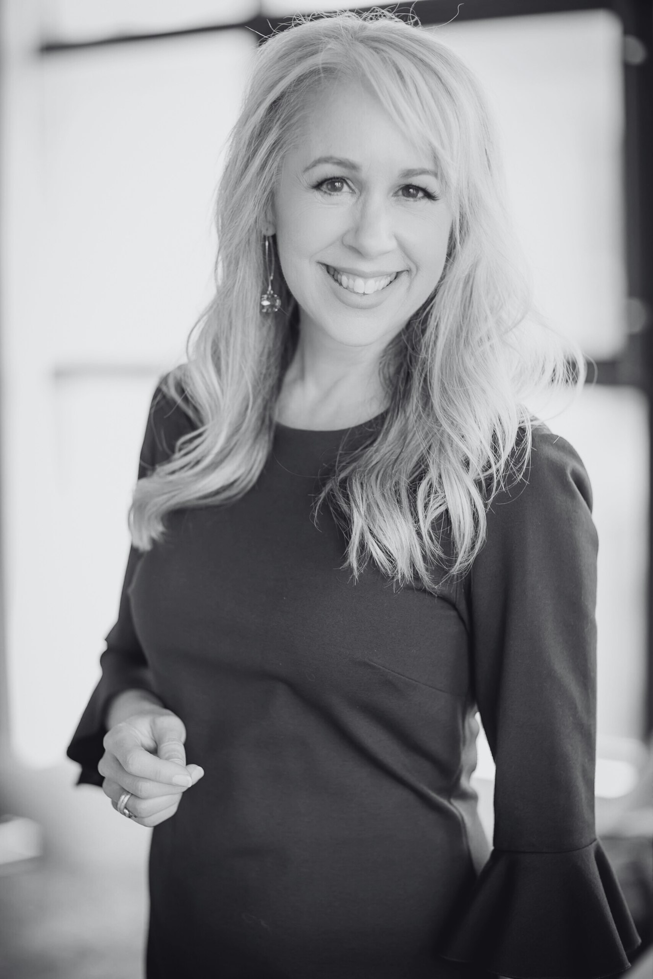 A woman with long hair smiling in a black dress, in a black and white portrait.