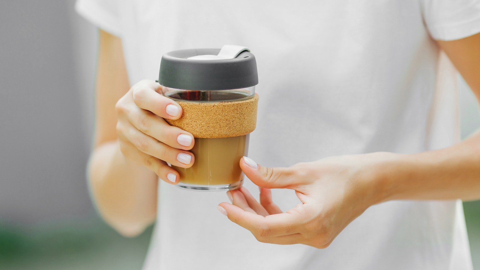 A person holding a cup with a lid and cork sleeve, containing coffee.