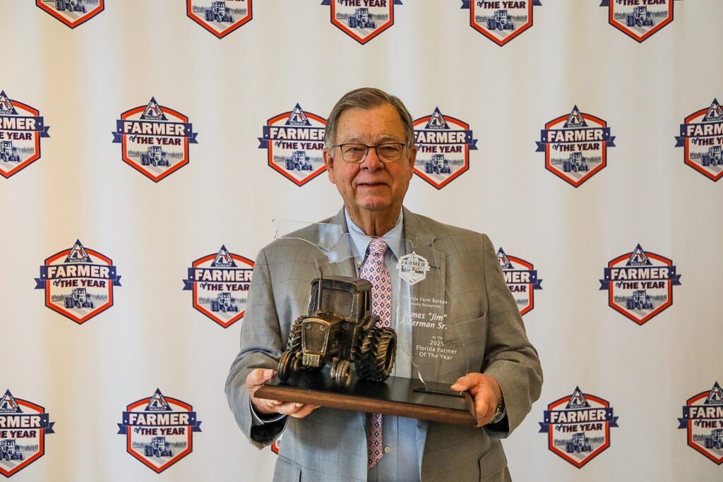 A person holding a "Farmer of the Year" award with a backdrop displaying the same logo.