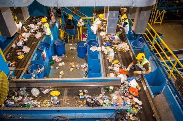 Workers sorting recycling on conveyor belts in a waste management facility.