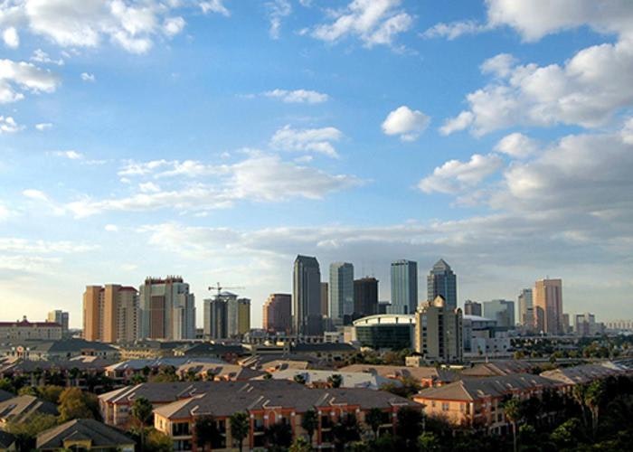 A city skyline with high-rise buildings, under a blue sky with clouds.