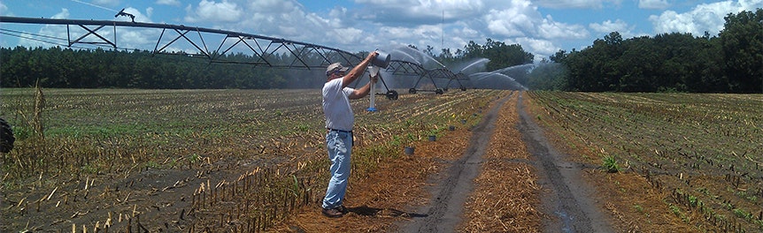 A person adjusts a large irrigation system in a farm field under a partly cloudy sky.