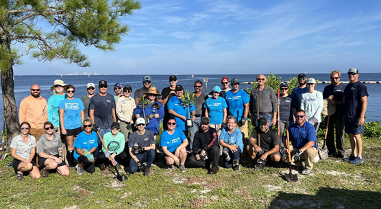 A group of people posing outdoors with water and trees in the background.