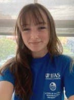 A person wearing a blue UF/IFAS Sea Grant T-shirt, smiling indoors with a window behind them.