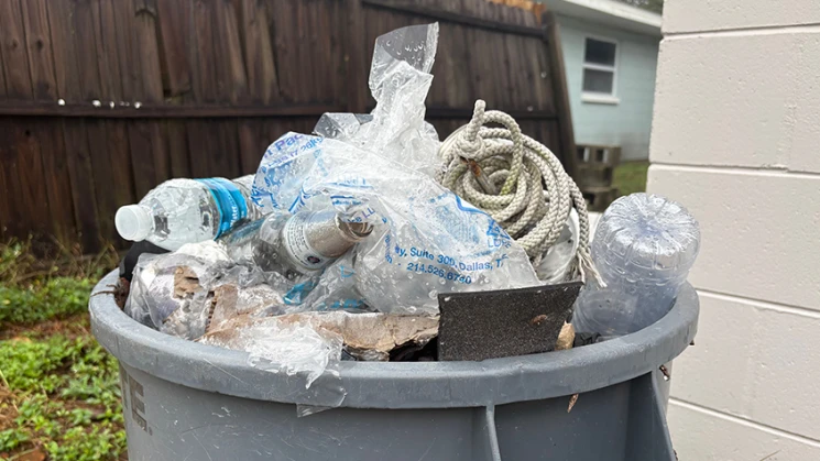 A trash bin filled with plastic bottles, packaging, rope, and other waste materials.