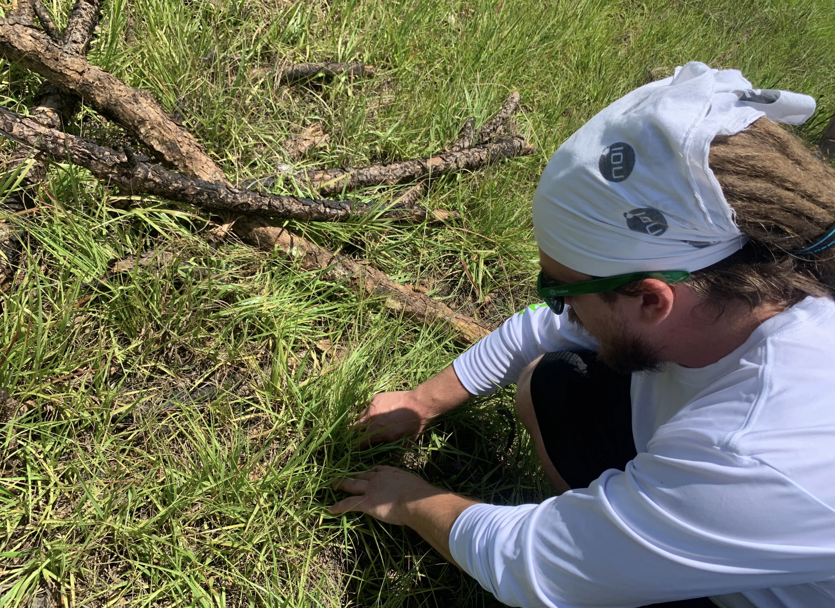 May contain: grass, plant, baseball cap, cap, clothing, hat, soil, vegetation, tree, wood, adult, male, man, person, land, nature, outdoors, woodland, photography, body part, finger, hand, accessories, glasses, face, head, and portrait