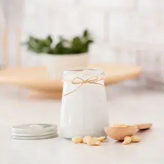 A jar of milk tied with twine beside almonds and a wooden spoon on a kitchen counter.