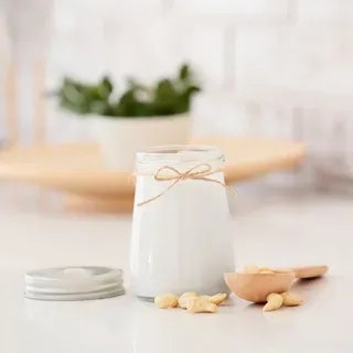 A jar of milk tied with twine beside almonds and a wooden spoon on a kitchen counter.