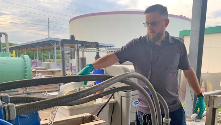 A man with gloves works with industrial equipment and hoses outdoors.