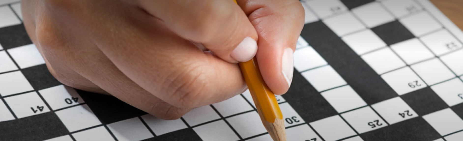 A hand with a pencil solving a crossword puzzle.