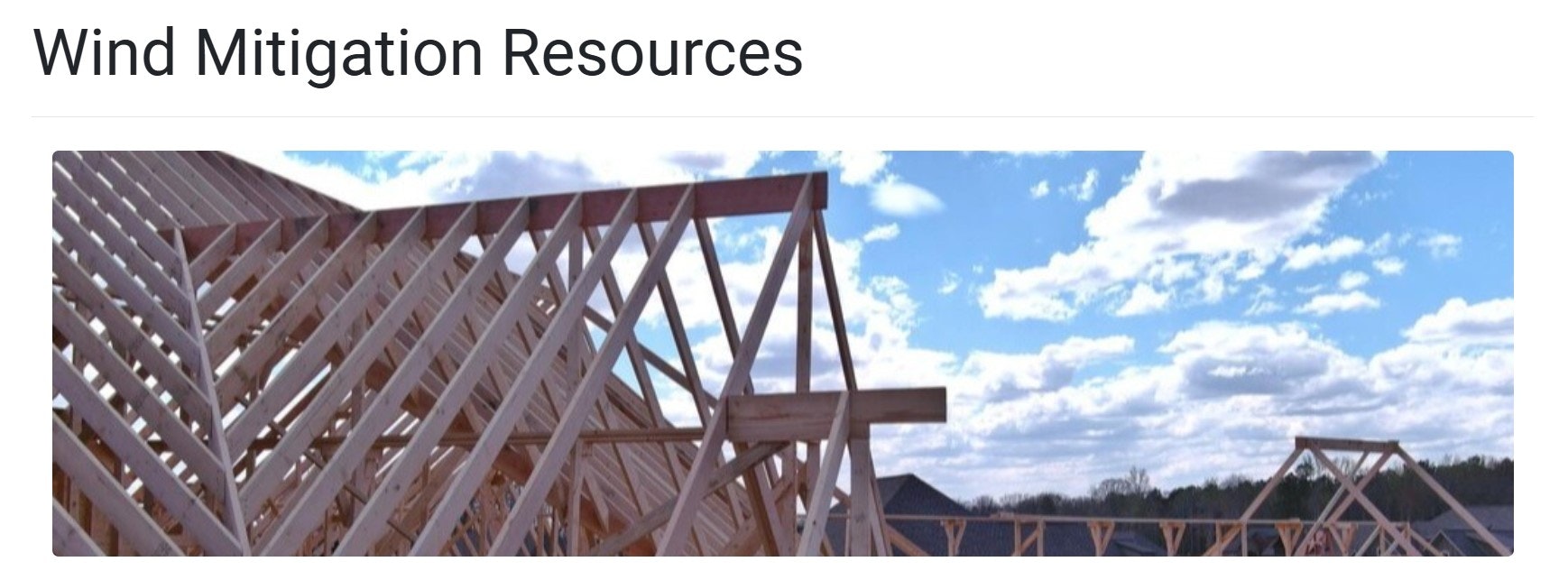 Wooden roof frame under construction with blue sky and clouds in the background.