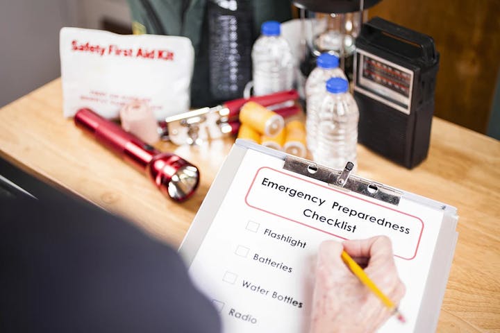 Emergency checklist, flashlight, radio, water bottles, and a first aid kit on a table, suggesting disaster preparedness.