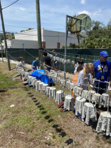 People working outside with cement structures on a wire fence, possibly engaged in a community or construction project.