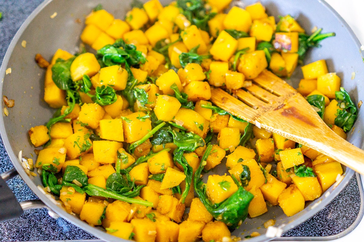 Sautéed butternut squash and spinach in a pan with a wooden spatula.