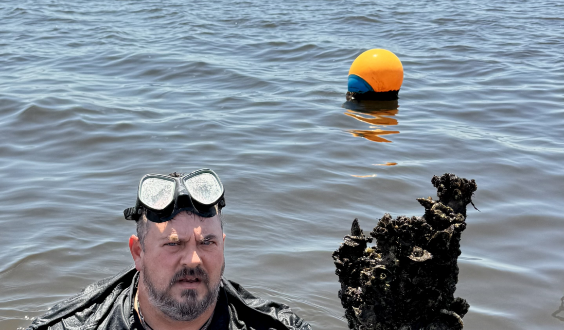 A person with goggles emerges from water near a buoy and a rock covered in barnacles.