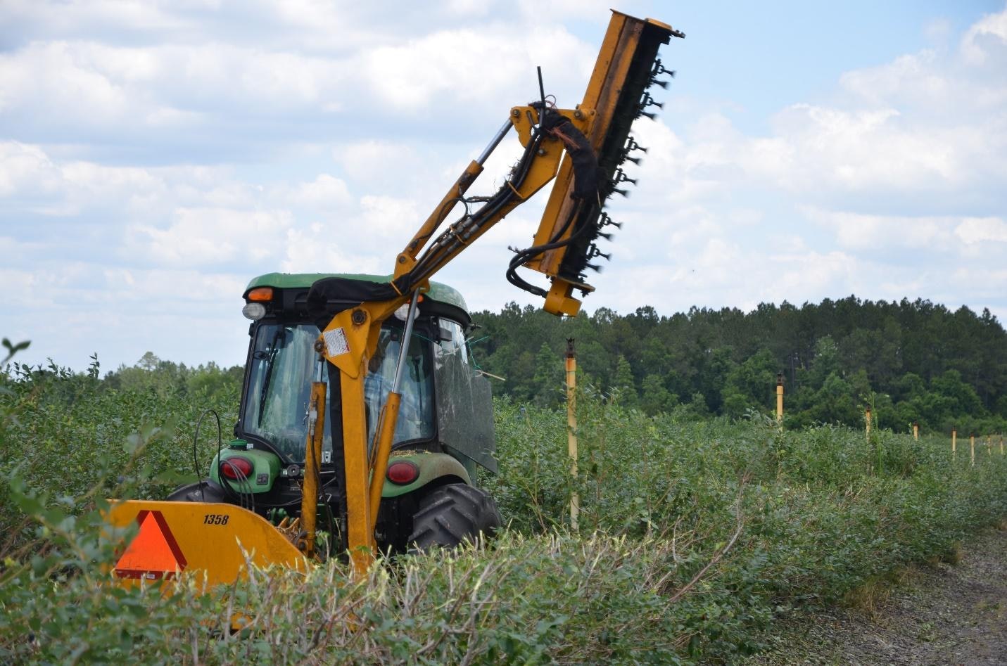 A tractor with an attached arm tool is trimming bushes in a field.