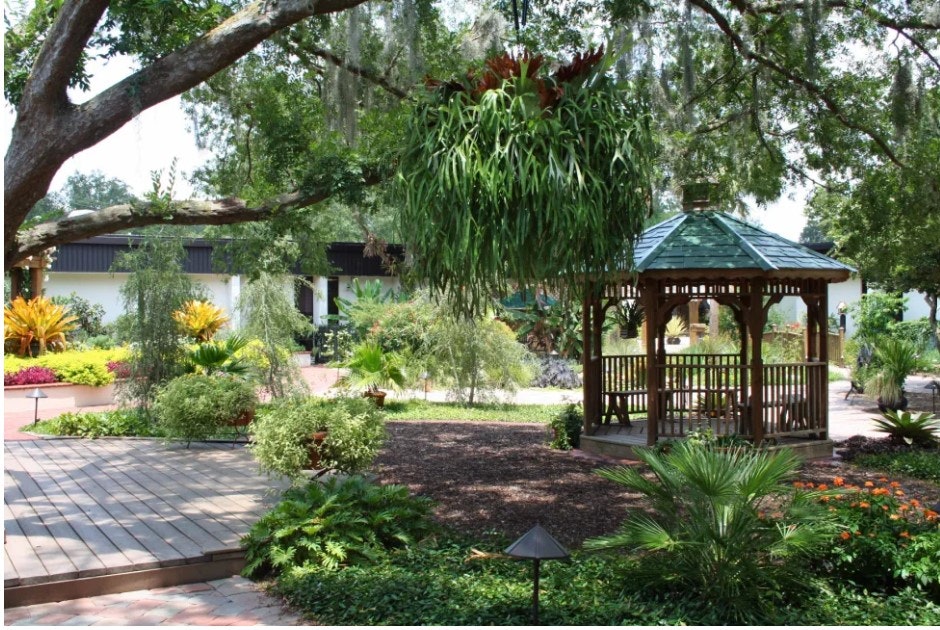 A serene garden with a gazebo, lush greenery, hanging plants, and a walking path.
