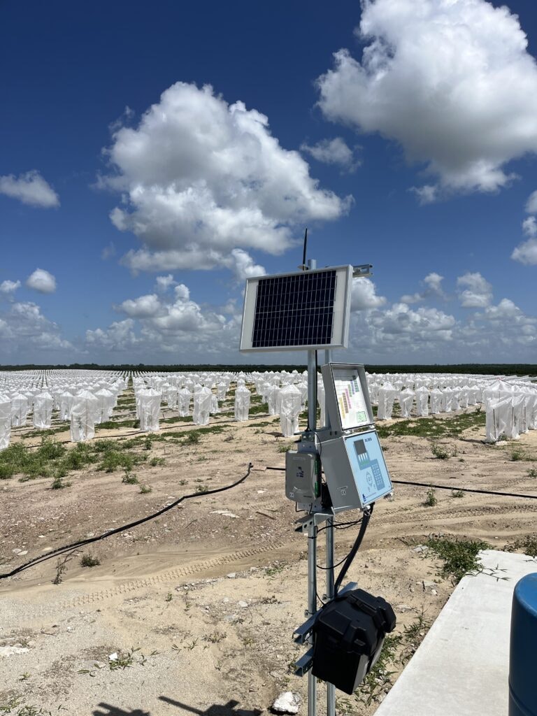Solar panel on equipment with agricultural field covered in white protective material under a blue sky with clouds.