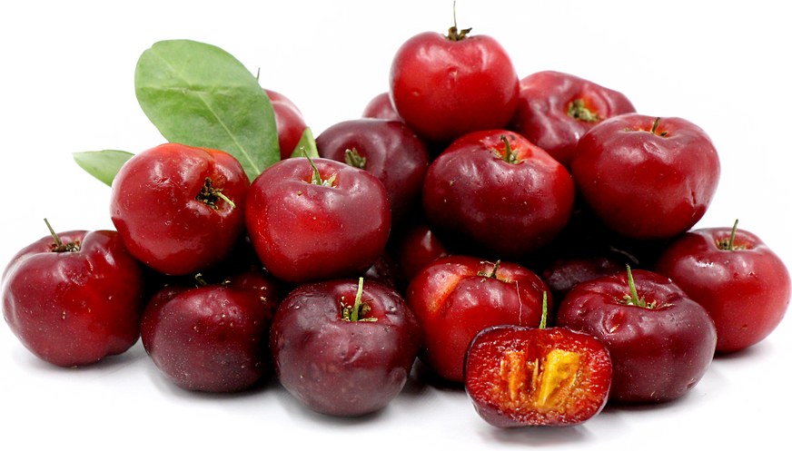 A pile of red acerola cherries, some with green leaves, one cut in half showing the yellow-orange interior.