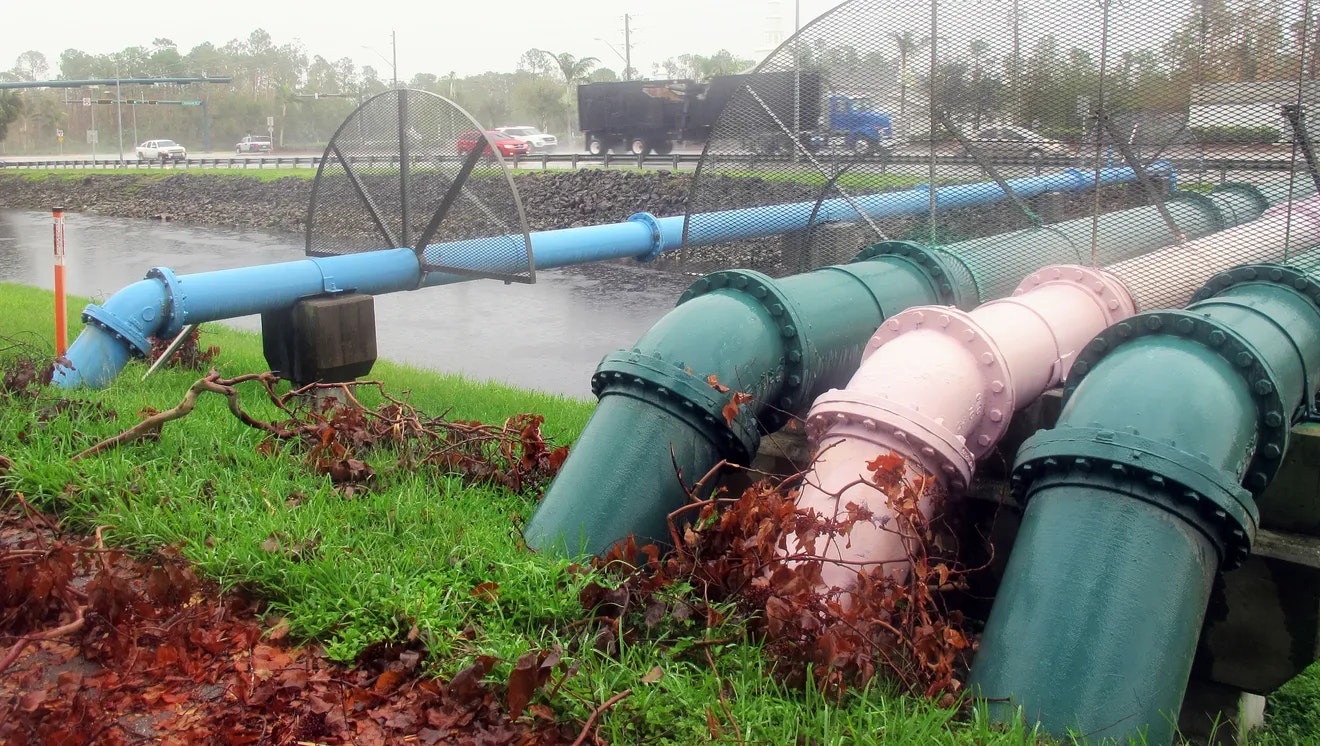 Large industrial pipes and a water pump near a road, possibly for drainage or water management, with vehicles in the background.