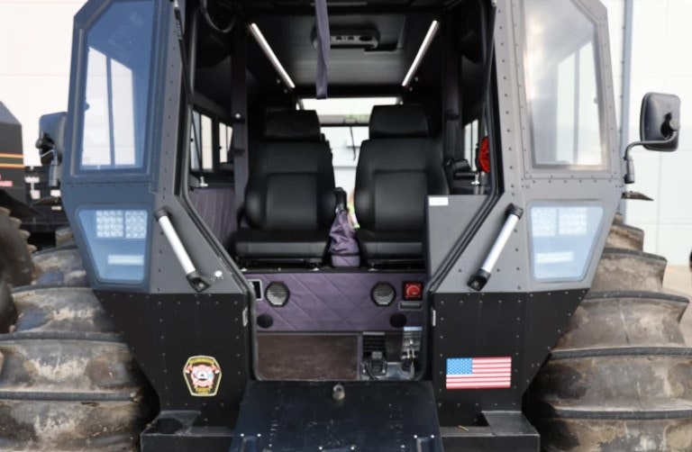 Interior of a large off-road vehicle with two seats, rugged tires, an American flag sticker, and a badge on the exterior.