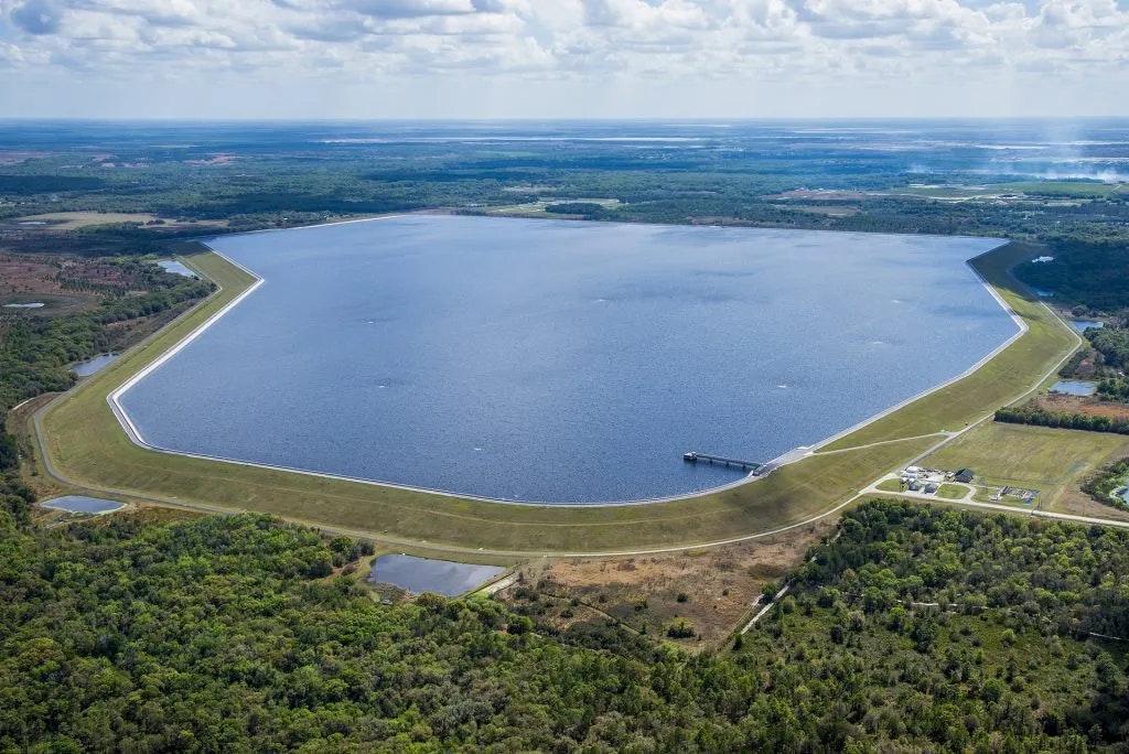 Aerial view of a large, rectangular reservoir with a dam, surrounded by forested land.