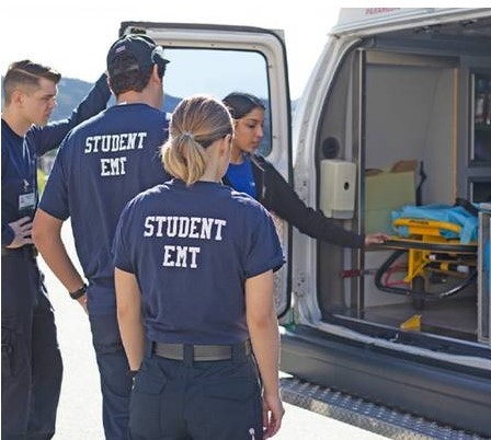 Three EMT students being shown how to properly remove a pram from ambulance