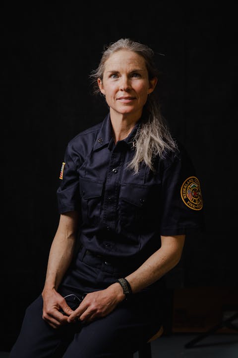 A woman in a fire department uniform sits confidently against a dark background.