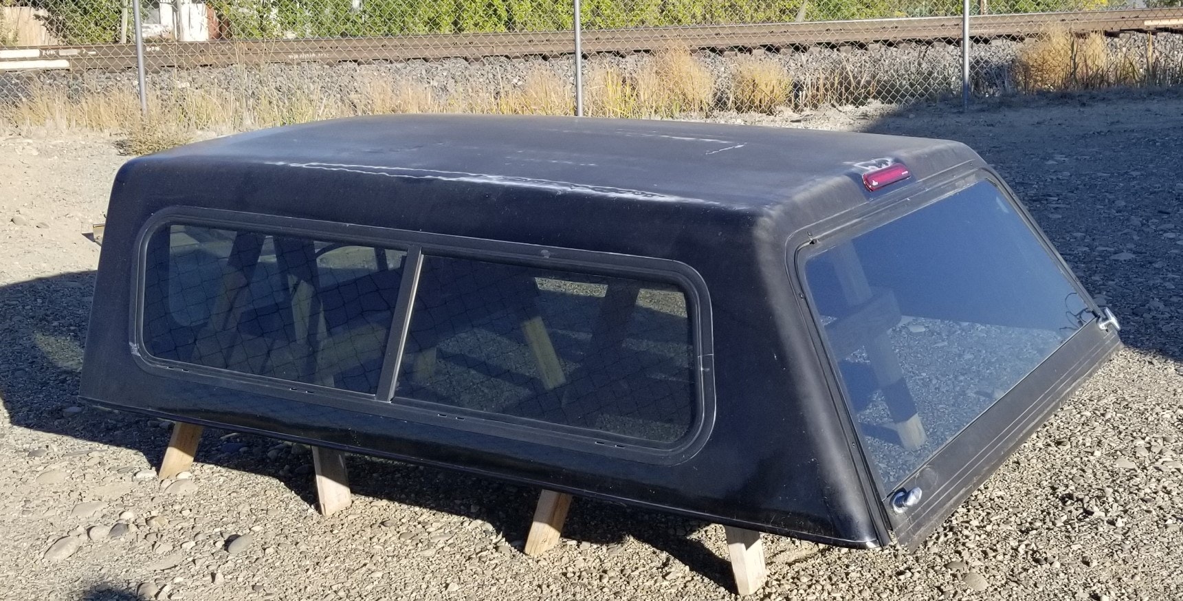 A detached black truck bed camper shell on a gravel surface.