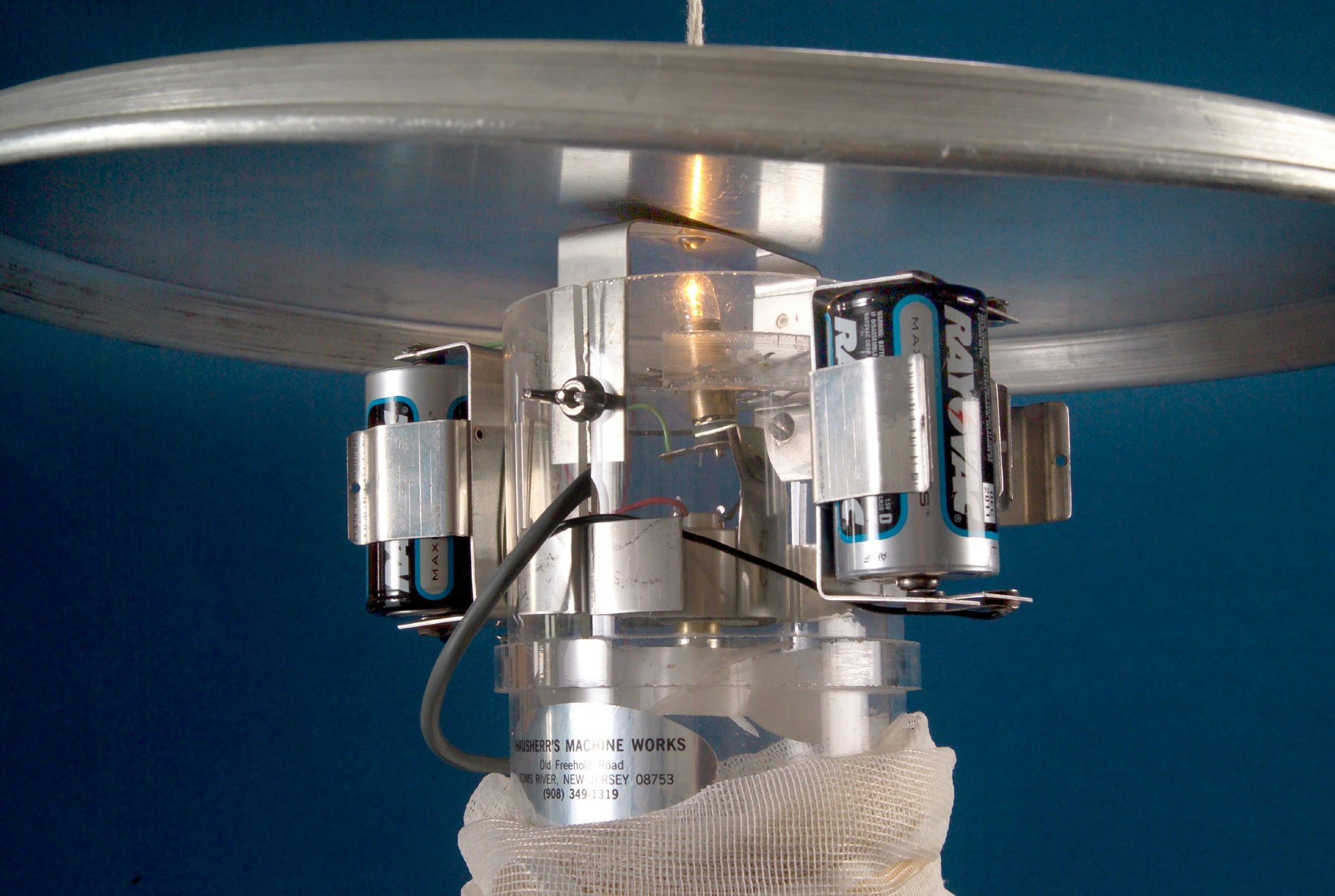 Mechanical device with batteries, wires, metal parts against a blue background. Appears complex, possibly a component of a machine.