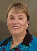 The image features a woman with short hair wearing a turquoise and black shirt, smiling at the camera.