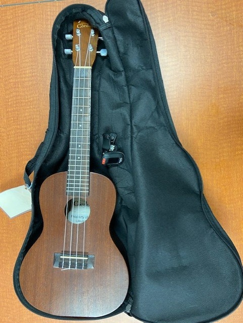 A ukulele in an open black soft case on a wooden surface.