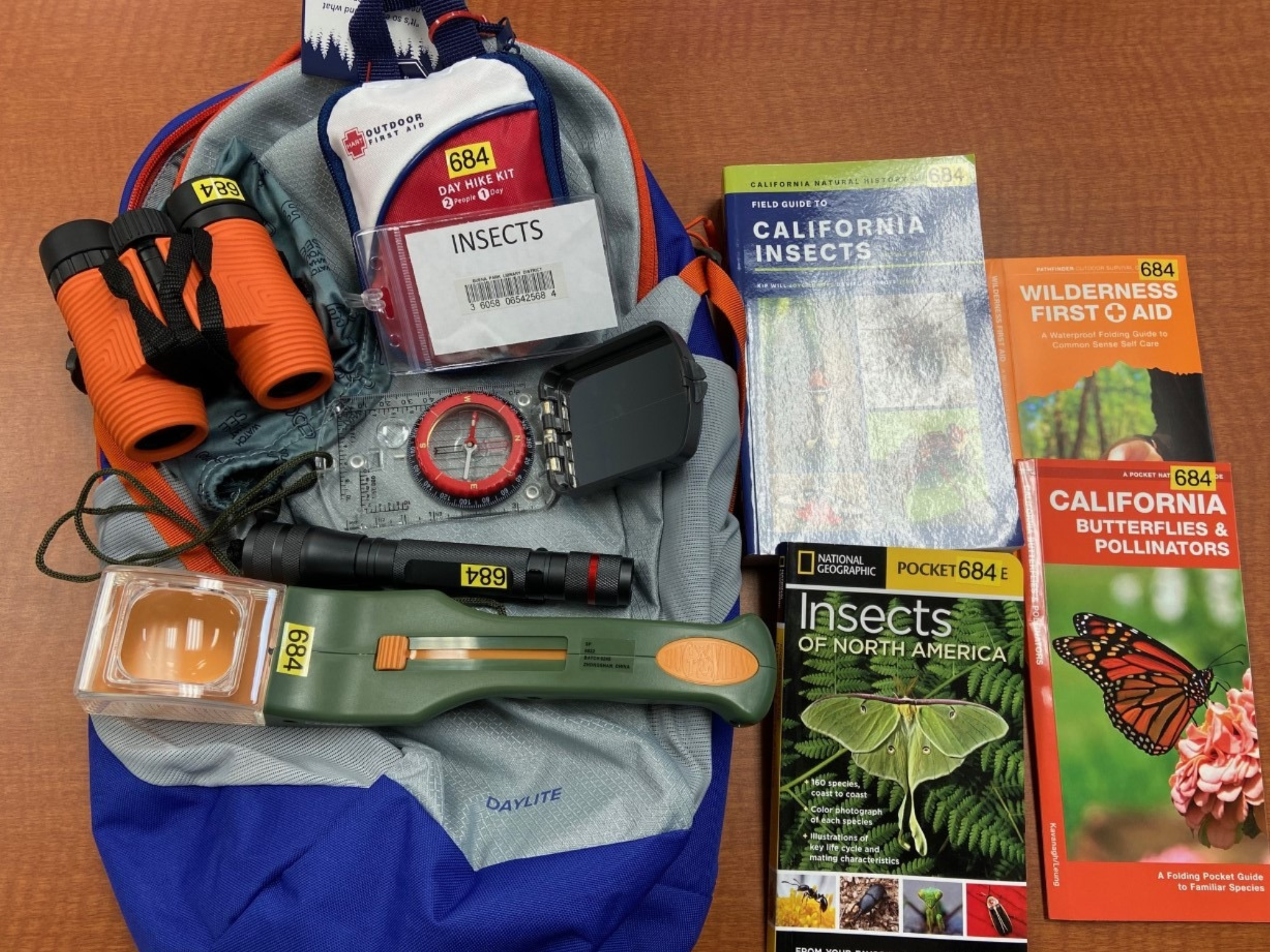 Backpack with first aid kit, binoculars, compass, flashlight, field guides on insects, and books on California nature and first aid.