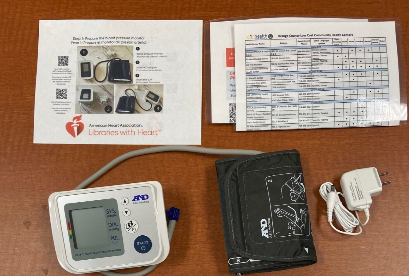 The image shows a blood pressure monitor, setup instructions, and a list of low-cost health centers in Orange County.