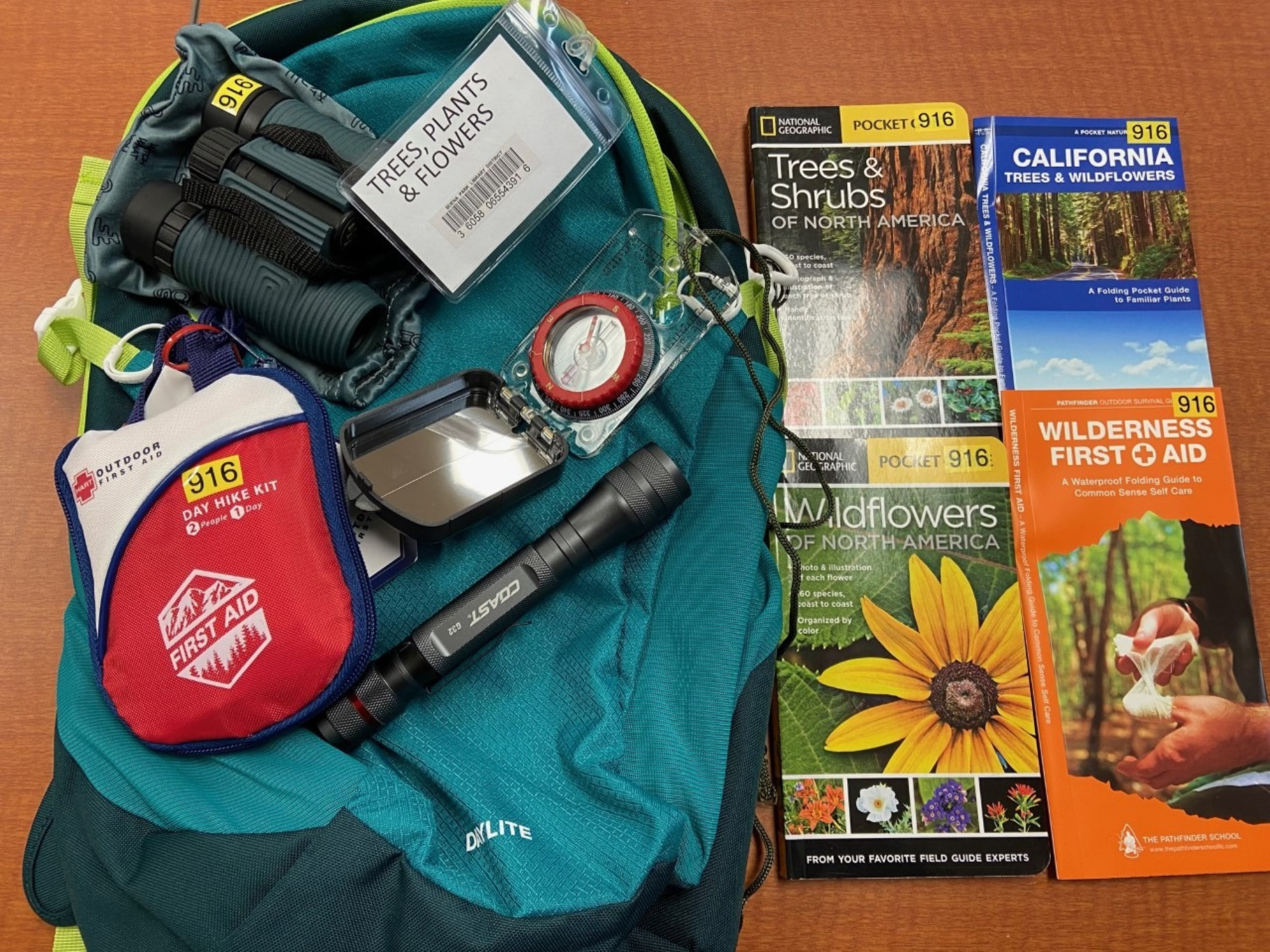 Hiking essentials: backpack, binoculars, first aid kit, compass, flashlight, mirror, plant guides, and wilderness first aid pamphlet.
