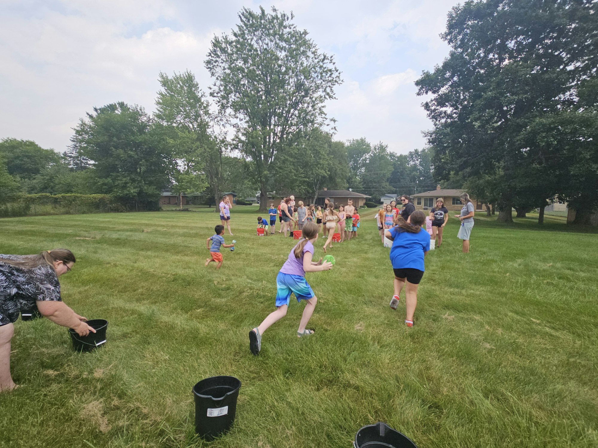 Group of children and adults playing with water balloons in a grassy field.