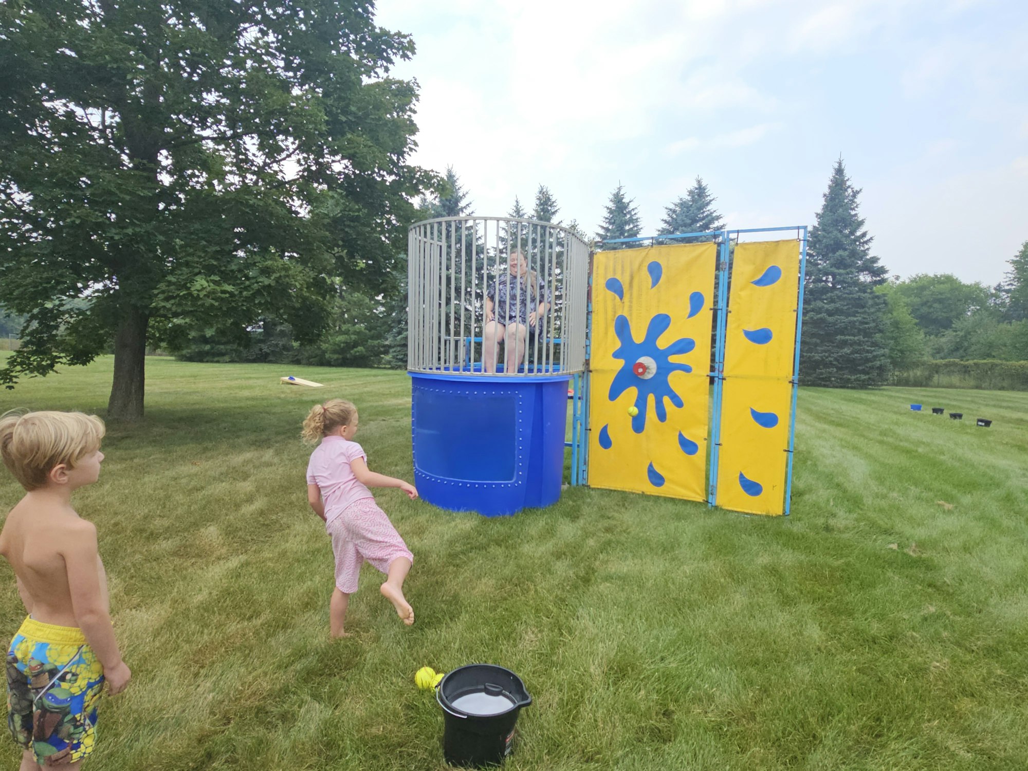 Kids playing with a dunk tank on a grassy field.