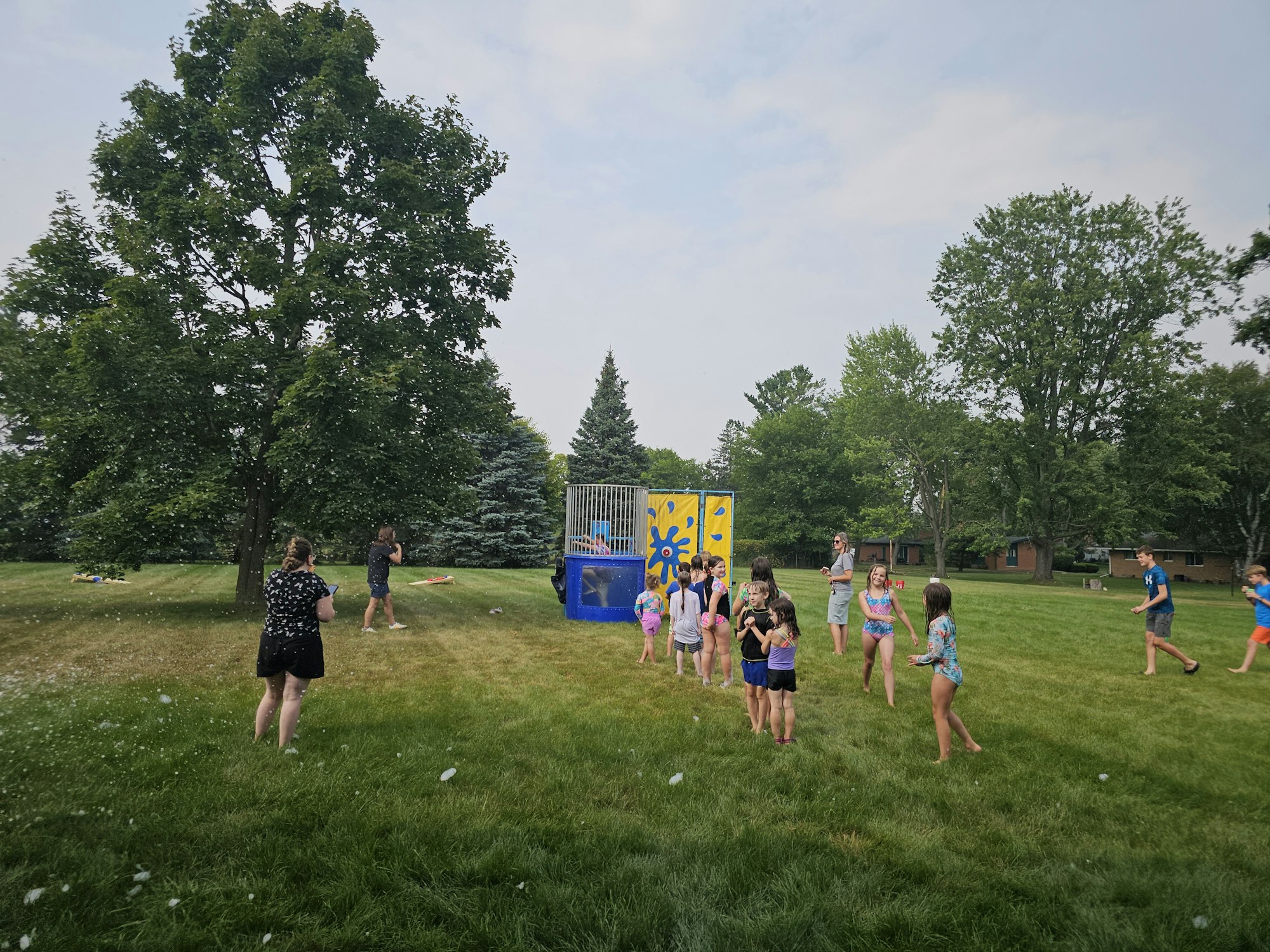 Group of kids playing on a grassy field with a dunk tank and trees in the background.