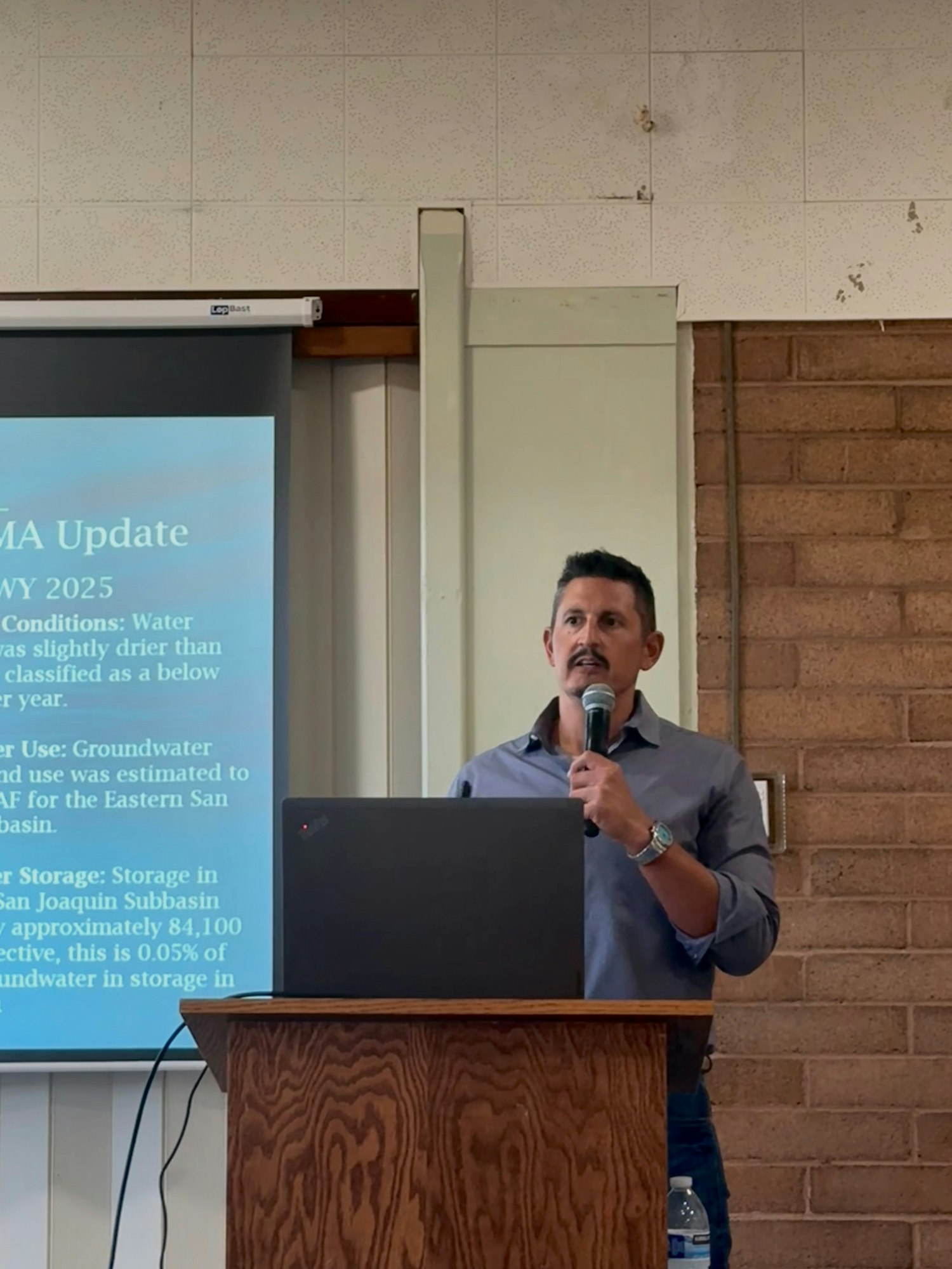 A presenter discusses water conditions and groundwater management at a meeting, with a projection screen displaying relevant data.