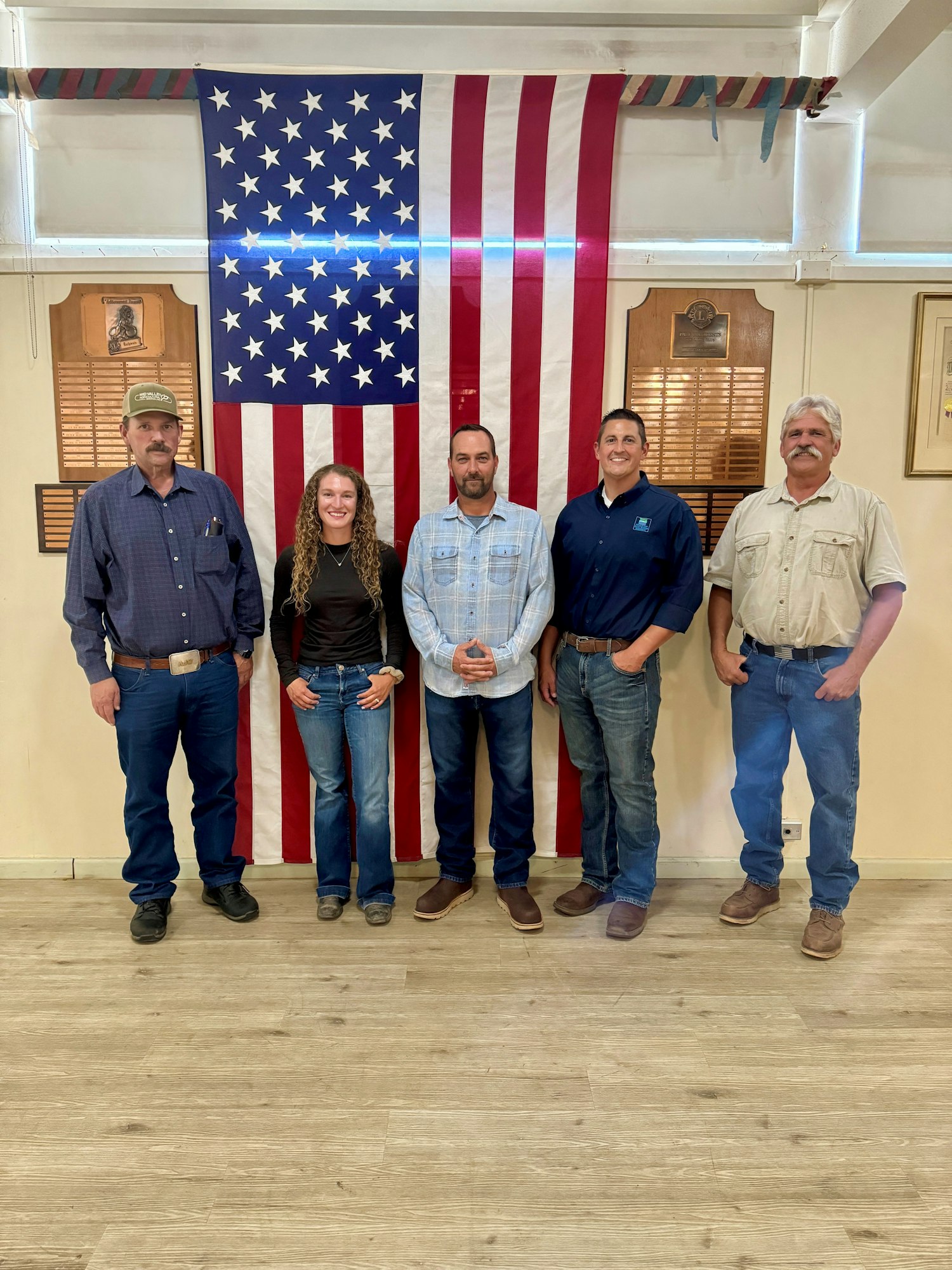 Five people standing in front of a large American flag indoors.