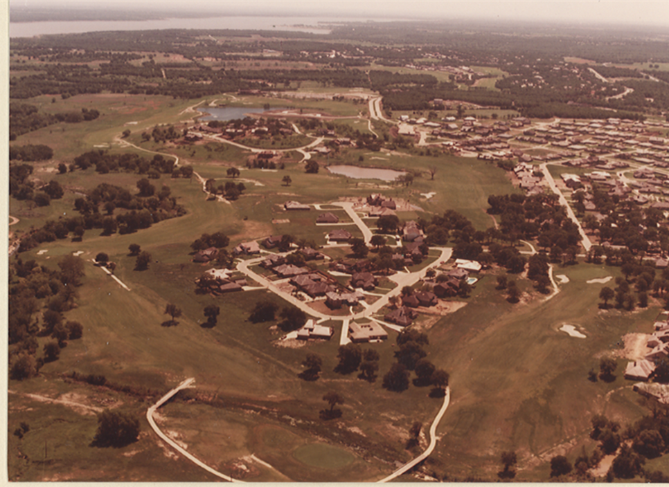 Aerial view of a residential area with scattered houses, roads, trees, and nearby water features.