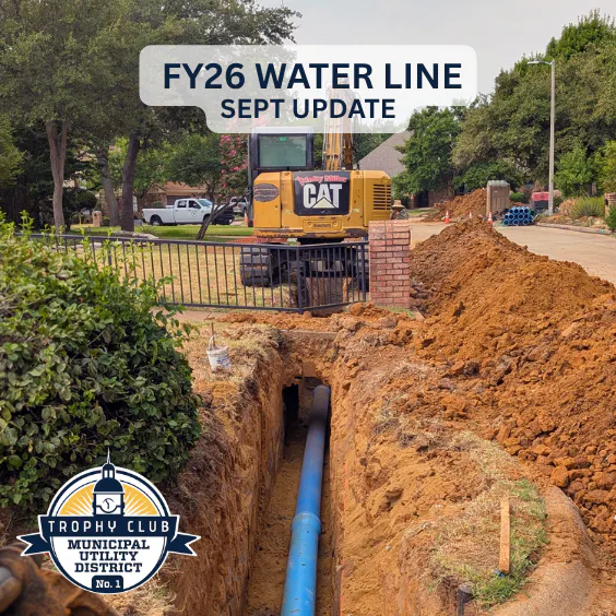 Construction update on the Trophy Club MUD FY26 water line project; showing a blue pipe in an excavated area with a machinery backdrop.