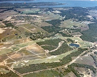 Aerial view of a rural landscape with fields, trees, a small body of water, and a lake in the distance.